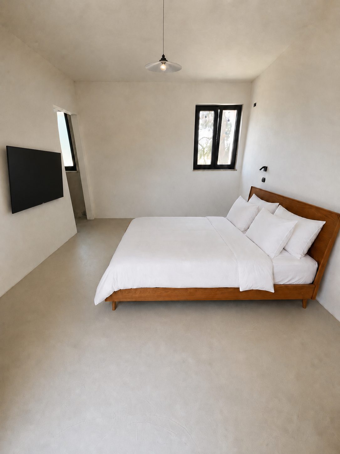 The first en-suite bedroom at Casa Andrea — microcement walls and floor in a warm tone, a wooden bed with white linen, a black-framed window, Puglia.