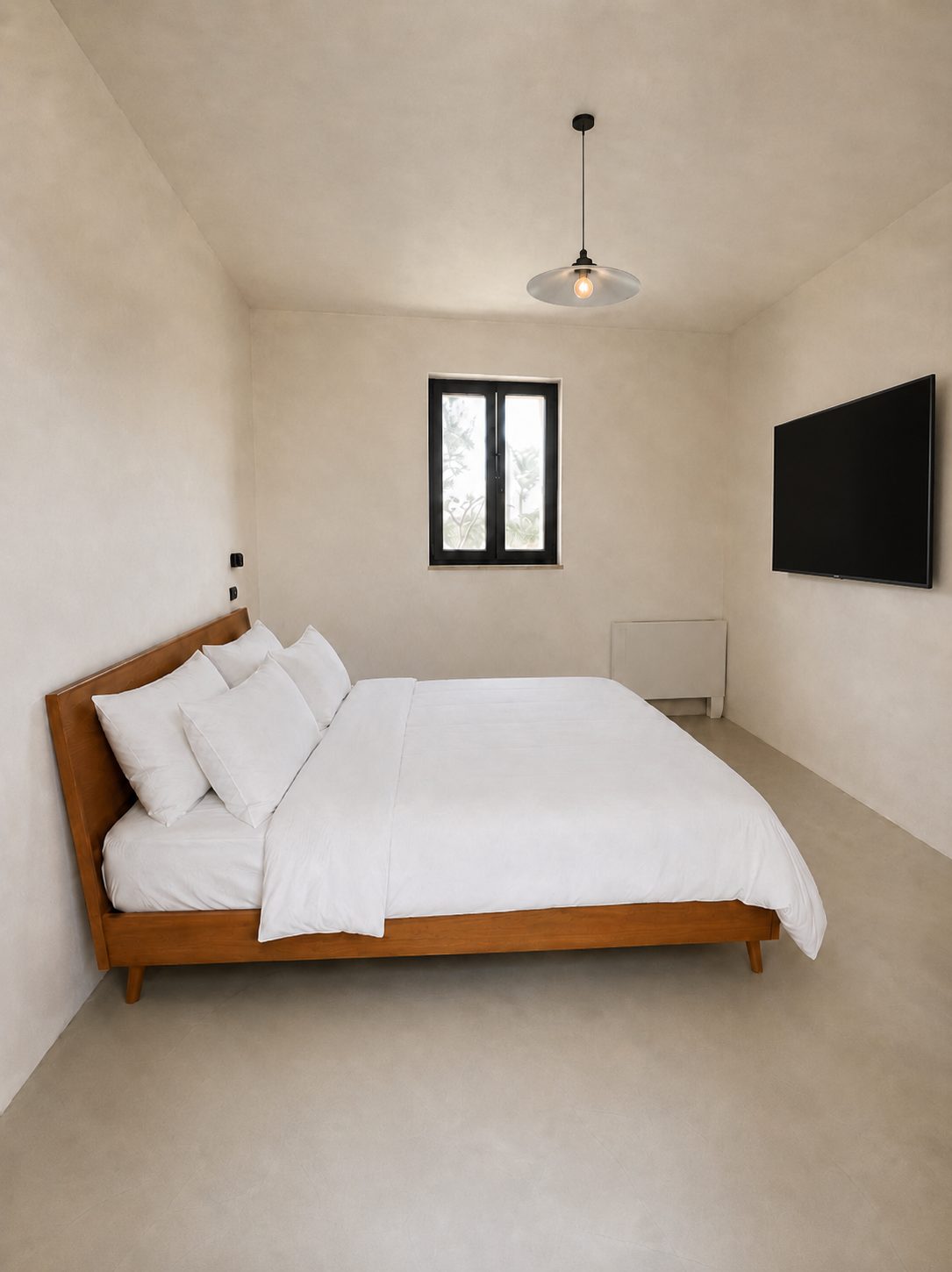 The second en-suite bedroom at Casa Andrea — the same microcement palette and wooden bed, a black-framed window, Puglia.