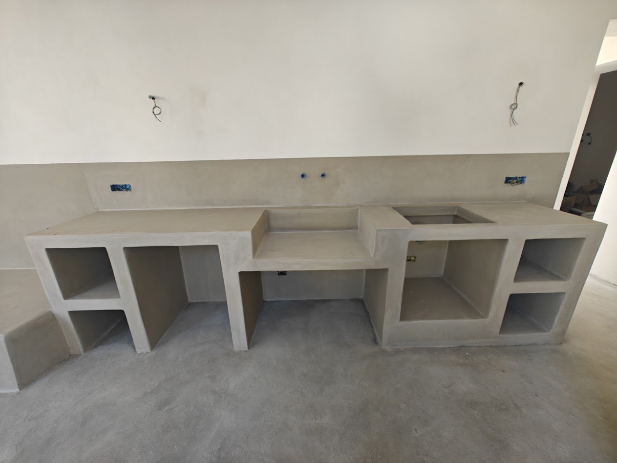 The stone kitchen counter in the new living wing of Casa Andrea — Pietra di Trani slab cut on site, built-in cooktop, lime-plaster wall behind, Puglia.
