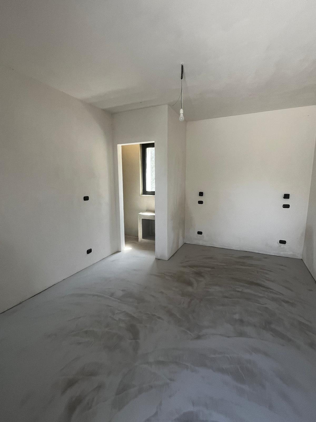 A new en-suite bedroom at Casa Andrea, near completion — lime-plaster walls, arched window onto the olive grove, lime-washed beams above.