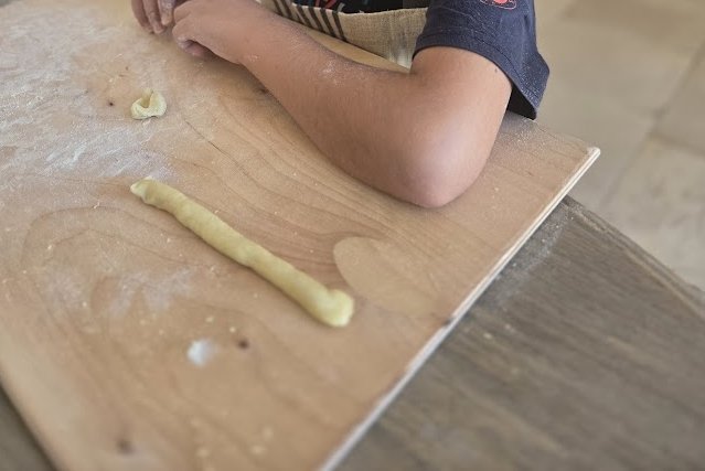 Hands shaping orecchiette on a wooden table at Casa Andrea — a slow morning of Pugliese pasta-making with a neighbour.