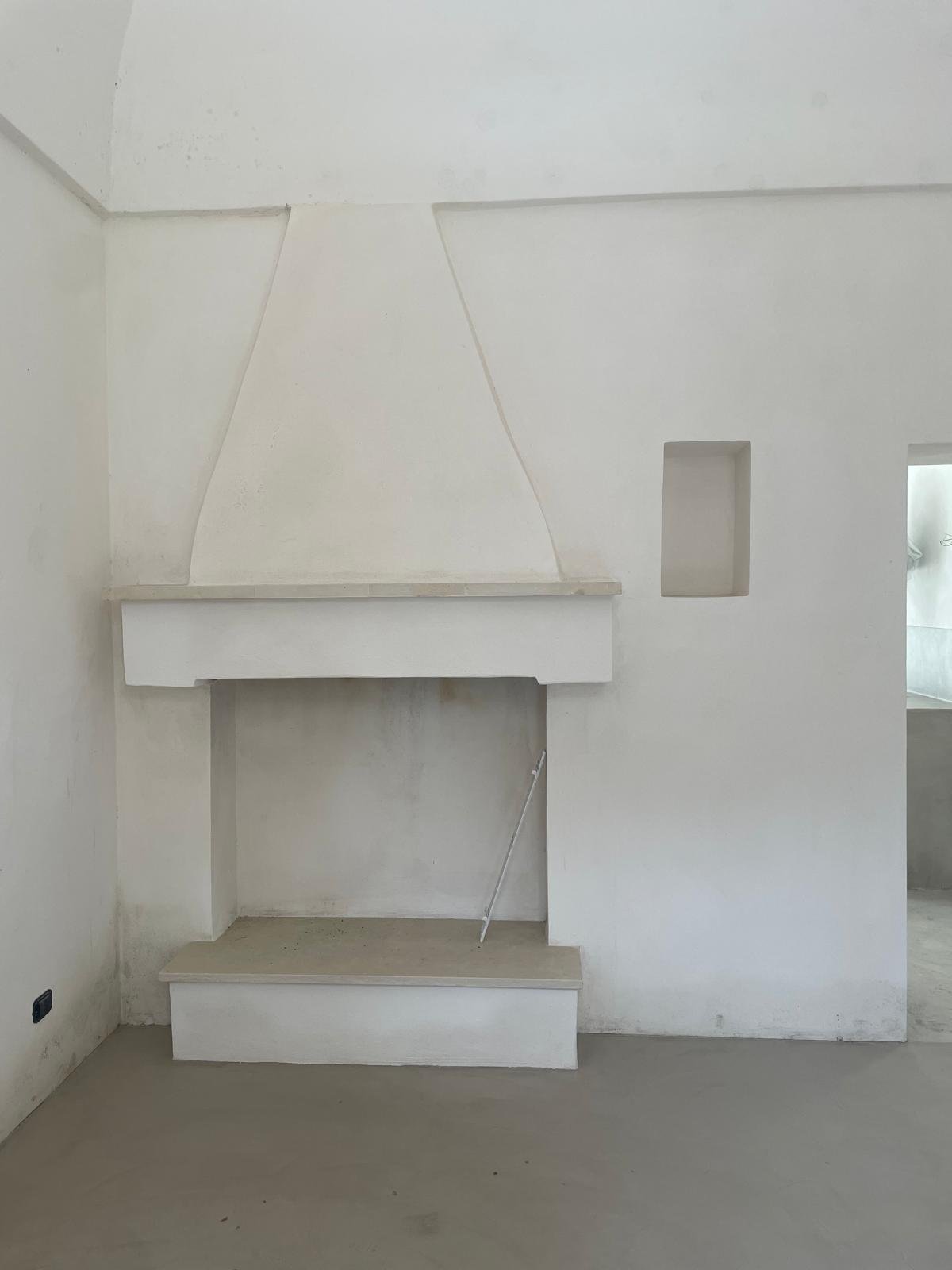 The restored fireplace in Casa Andrea's casale, March 2026 — classic Pugliese conical white-plaster hood, Pietra di Trani lintel and hearth, built-in panca camino bench, niche carved into the wall.