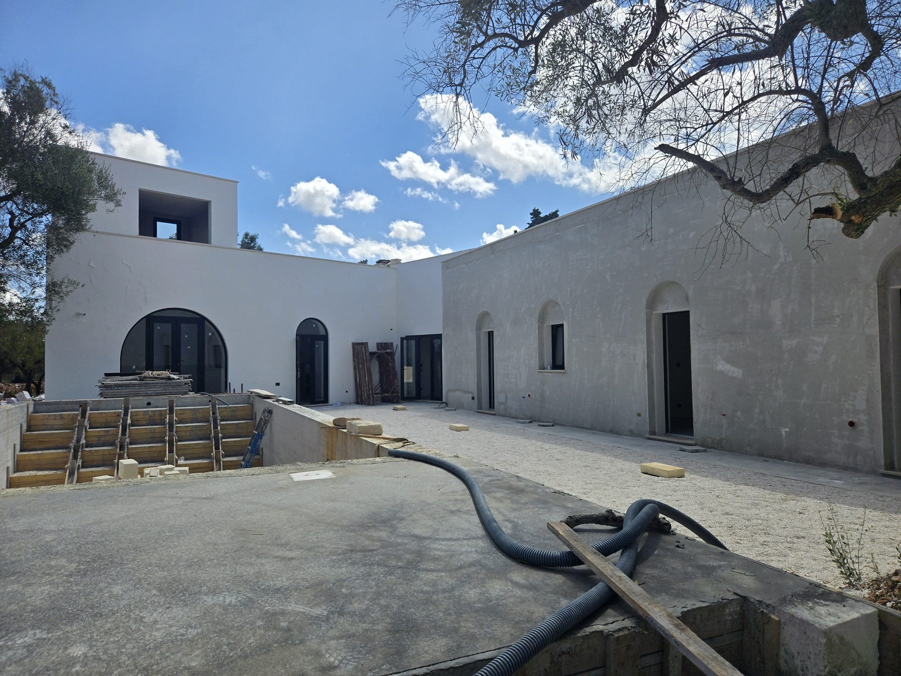 L'extérieur de la villa Casa Andrea dans les Pouilles, fin d'été 2025 — murs chaulés, arches posées, la cour intérieure entre la vieille voûte et la nouvelle aile.